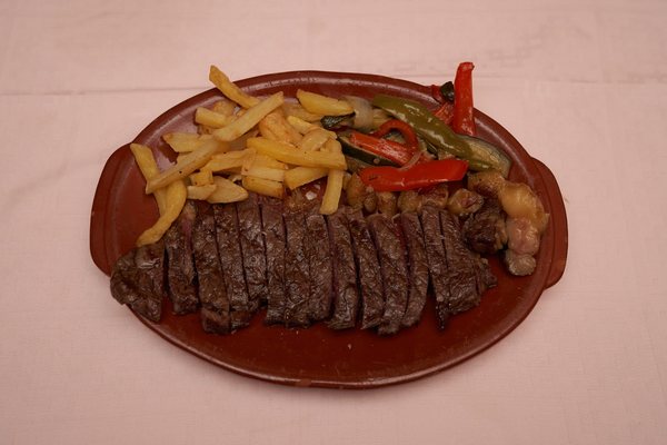 Carne de vacuno a la brasa, trinchada, con patatas fritas y pimientos en fuente de barro
